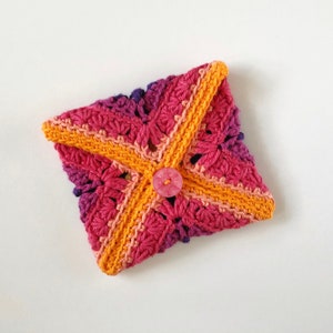 May include: A crocheted envelope-style pouch with a pink, orange, and purple ombre design. The pouch has a button closure and is made with a textured stitch.