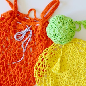 May include: Three crocheted bags in orange, yellow, and green. The orange bag has a gray drawstring and is a mesh style. The yellow and green bags have tassels.