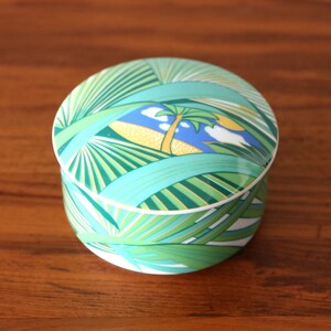 Puede incluir: Una caja de cer&aacute;mica redonda para baratijas con un dise&ntilde;o de palmera tropical verde, azul y amarillo.