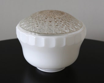 May include: A white glass light fixture with a clear, patterned top. The fixture has a rounded shape with a wide base and a textured, geometric design on the top. The fixture is sitting on a black surface.