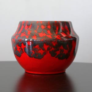 May include: A vibrant red ceramic bowl with a unique glaze. The bowl features a striking pattern of black and gray accents near the rim, creating a bold contrast. The design is a perfect accent piece for any home decor.
