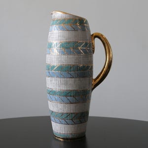 May include: A decorative ceramic jug with a gold handle and rim. The body features a pattern of white, teal, and gold horizontal stripes. The jug is a stylish addition to any home.