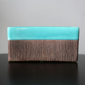 Puede incluir: Un macetero rectangular de cerámica con un esmalte turquesa en la parte superior y un esmalte texturizado marrón en la parte inferior.