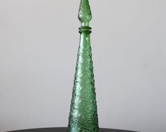 May include: A tall, green glass bottle with a pointed top and a swirling pattern. The bottle is on a black surface.