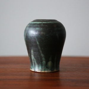 May include: A small, dark green and black ceramic vase with a rounded body and a slightly flared lip.