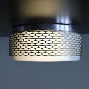 May include: A white ceiling light fixture with a metal mesh shade. The light is on and casting a warm glow.