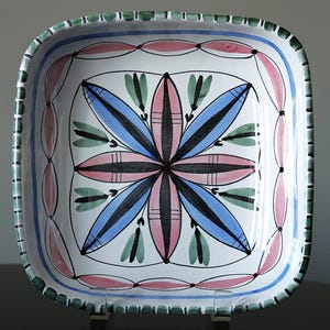 Puede incluir: Plato cuadrado de cerámica para servir con un diseño floral pintado a mano. El plato presenta una base blanca con un motivo floral central en azul, rosa y negro. El borde tiene un patrón verde y rosa, con un contorno azul.