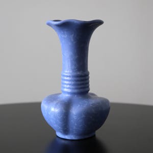 May include: A blue ceramic vase with a fluted rim and a bulbous base. The vase has a textured surface and a cylindrical neck with horizontal ridges. The vase is approximately 8 inches tall.
