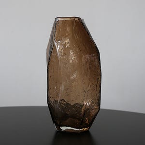 K&ouml;nnte beinhalten: Eine braune Glasvase mit einem einzigartigen, facettierten Design. Die Vase hat eine strukturierte Oberfl&auml;che mit kleinen Blasen, die f&uuml;r visuelles Interesse sorgen. Die Vase ist ein dekorativer Artikel, geeignet f&uuml;r Blumen oder als eigenst&auml;ndiges Kunstwerk.
