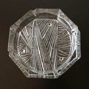 Puede incluir: Un cenicero de vidrio transparente con un diseño geométrico. El cenicero tiene una forma octogonal y una superficie texturizada.