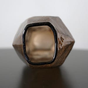 K&ouml;nnte beinhalten: Eine braune, facettierte Glasvase mit dunklem Rand. Die Vase hat eine strukturierte Oberfl&auml;che und eine geometrische Form. Das Innere der Vase ist sichtbar. Der Hintergrund ist neutral.