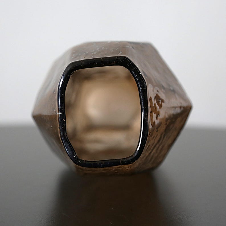K&ouml;nnte beinhalten: Eine braune, facettierte Glasvase mit dunklem Rand. Die Vase hat eine strukturierte Oberfl&auml;che und eine geometrische Form. Das Innere der Vase ist sichtbar. Der Hintergrund ist neutral.
