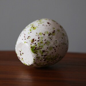 May include: White ceramic egg-shaped vase with brown and green speckled paint.