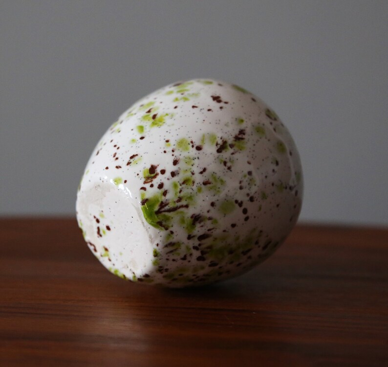 May include: White ceramic egg-shaped vase with brown and green speckled paint.