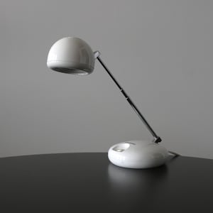 May include: A white desk lamp with a rounded shade and base, connected by a silver adjustable arm. The lamp is designed with a modern aesthetic, suitable for a home office or bedside table.