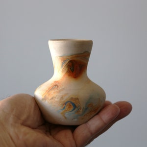 May include: A small, hand-painted ceramic vase with a light brown base and swirling blue, orange, and yellow accents.