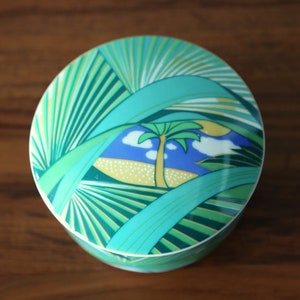 Puede incluir: Una caja de cer&aacute;mica redonda con un dise&ntilde;o verde, azul y amarillo de palmeras y una escena tropical.