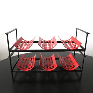 May include: A two-tiered red and black metal wine rack with six slots for bottles. The rack has a geometric design on the bottle holders.