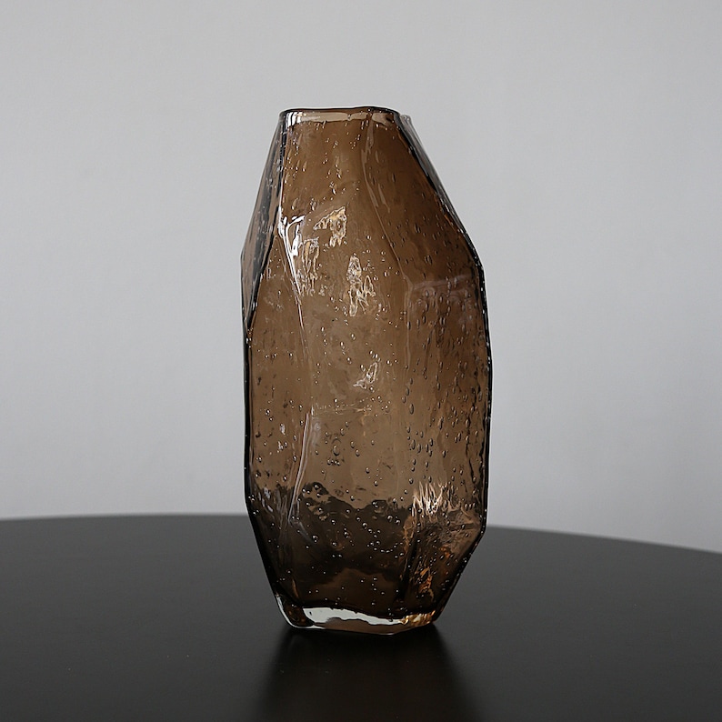 K&ouml;nnte beinhalten: Eine braune Glasvase mit einem einzigartigen, facettierten Design. Die Vase hat eine strukturierte Oberfl&auml;che mit kleinen Blasen, die f&uuml;r visuelles Interesse sorgen. Die Vase ist ein dekorativer Artikel, geeignet f&uuml;r Blumen oder als eigenst&auml;ndiges Kunstwerk.