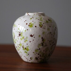May include: White ceramic vase with a speckled glaze in shades of green and brown.