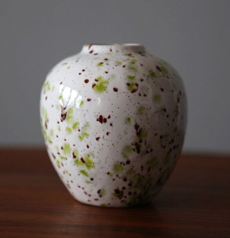 May include: White ceramic vase with a speckled glaze in shades of green and brown.