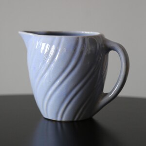 Könnte beinhalten: Ein hellblauer Keramik-Milchkännchen mit einem Wirbelmuster. Der Milchkännchen hat einen Griff und einen Ausguss.