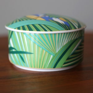 Puede incluir: Una caja de porcelana redonda para baratijas con un dise&ntilde;o de hojas tropicales verdes, amarillas y azules.