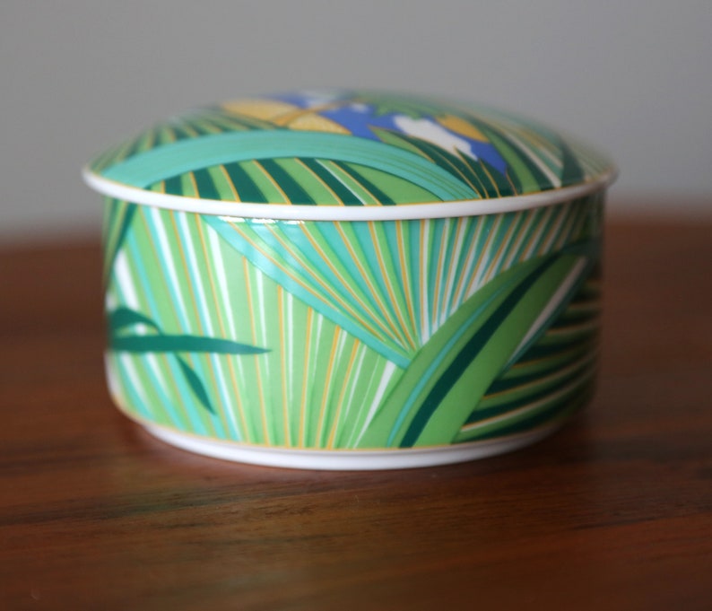 Puede incluir: Una caja de porcelana redonda para baratijas con un dise&ntilde;o de hojas tropicales verdes, amarillas y azules.