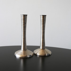 May include: A pair of silver candlestick holders with a ridged design. The holders are on a black surface.