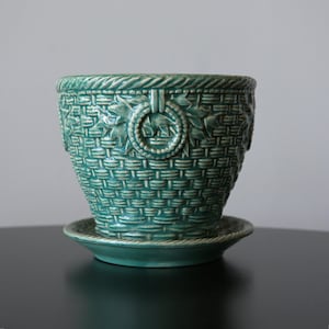 May include: A teal ceramic planter with a matching saucer, featuring a raised basket-weave texture, a rope-style rim, and a decorative circular ring motif embossed on the exterior surface. The glazed finish has subtle variations in color depth.