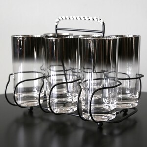 May include: A set of six silver-rimmed glass tumblers in a black metal holder with a white and black striped handle.