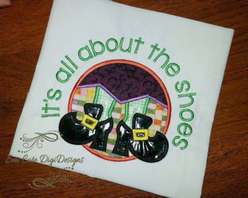 May include: White t-shirt with green embroidery that reads "It's all about the shoes". The embroidery includes two black witch shoes with green buckles and a purple and green background.