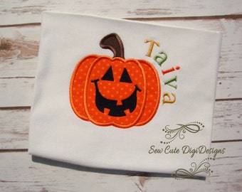 May include: White t-shirt with an orange pumpkin with a smiling jack-o'-lantern face and the name "Taiva" embroidered in green, yellow, and orange. The text "Sew Cute Digi Designs" is also embroidered on the shirt.