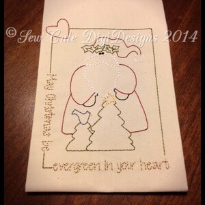 May include: A white fabric card with a red heart in the top left corner. The card has a green frame with a stitched image of Santa Claus holding a star on a tree. The text "Sew Cute Digi Designs 2014" is in the top right corner. The text "May your Christmas be...evergreen in your heart" is stitched in the bottom of the frame.