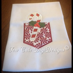May include: White fabric with a red and white candy cane and holly embroidery design in a red and white peppermint pocket. The text "Sew Cute Digi Designs ©" is below the design.