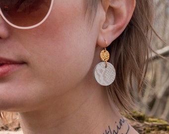 Peut inclure: Une personne avec des cheveux courts, coupés en brosse, châtain clair, portant des lunettes de soleil roses et un pull marron. Elle a un tatouage sur le cou qui dit "Nothing" et un autre tatouage sur l'épaule. Elle porte une paire de boucles d'oreilles en or avec un charme rond blanc texturé.