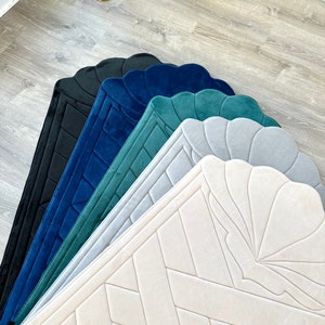 May include: Five prayer rugs in different colors, including black, navy blue, teal, light gray, and cream. The rugs have a scalloped edge and a geometric pattern.