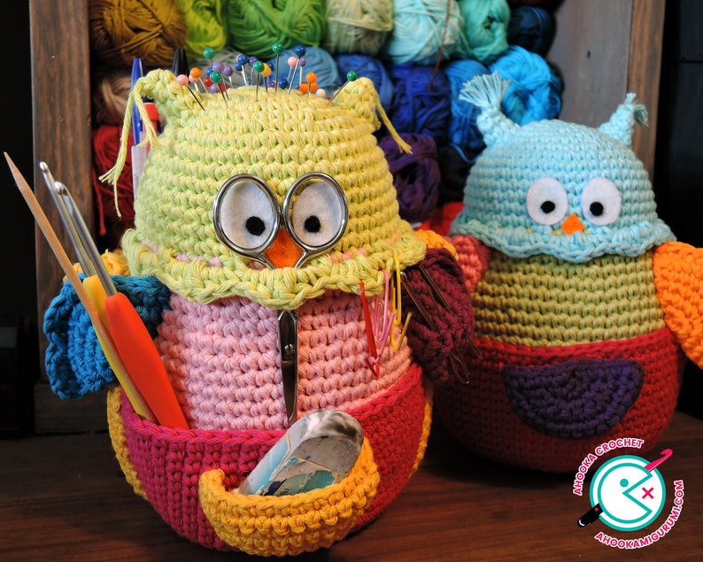 May include: Two crocheted owl-shaped containers, one in pink, green, and yellow with a variety of sewing needles and tools inside, and the other in blue, green, and purple. Both owls have large black eyes and a small orange beak.