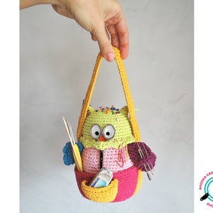May include: A crocheted owl-shaped bag with a yellow handle. The bag is filled with colourful yarn, needles, and pins. The owl has large, round eyes and a pink beak.