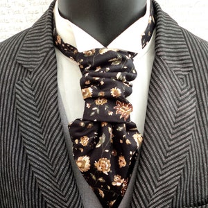 Puede incluir: Una corbata negra con un estampado floral en tonos marrones y beige. La corbata está anudada y se lleva sobre una camisa blanca y una chaqueta de traje gris.