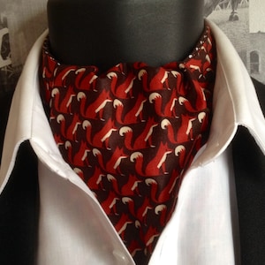 May include: An ascot with a repeating pattern of red foxes on a dark brown background. The ascot is worn with a white collared shirt and a black suit jacket. The fox pattern is a stylish accessory, suitable for formal or smart casual wear.