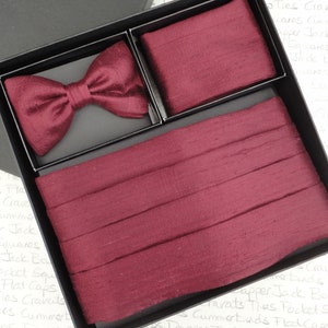May include: A burgundy silk bow tie and matching cummerbund set in a black box. The bow tie is made of a soft, luxurious silk and has a classic shape. The cummerbund is a wide band that can be worn around the waist.