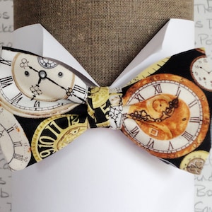 Peut inclure: Un nœud papillon noir avec un fond blanc orné d'un motif répété de cadrans d'horloges anciennes. Les cadrans d'horloges ont des chiffres romains et des accents dorés.