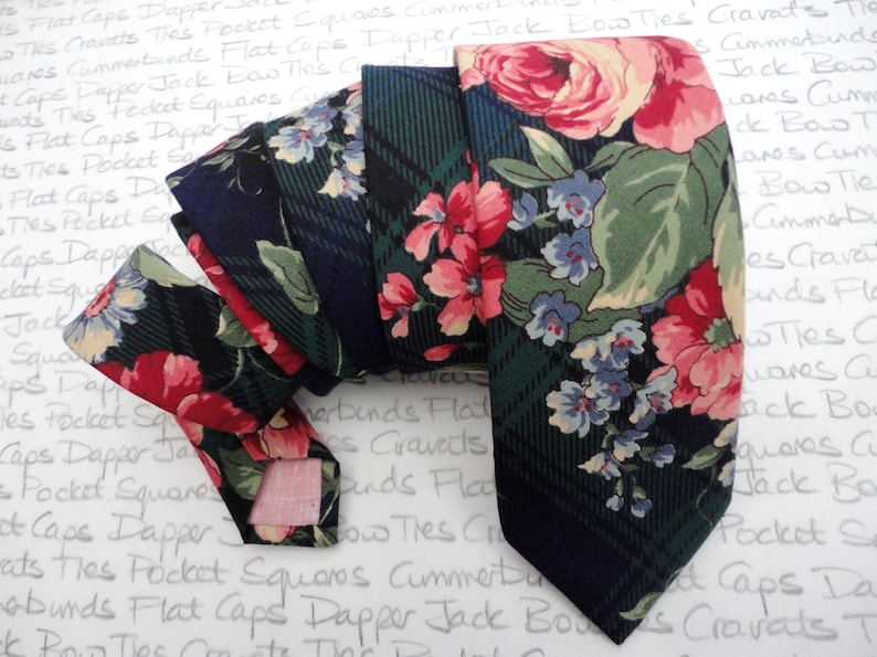 May include: A dark blue and green patterned tie with a floral design. The tie features pink, blue, and white flowers on a dark background.