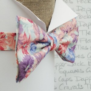May include: A floral patterned bow tie with pink, purple and blue flowers on a white background.