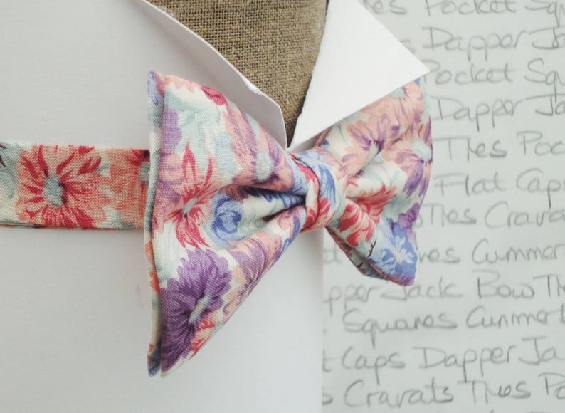 May include: A floral patterned bow tie with pink, purple and blue flowers on a white background.