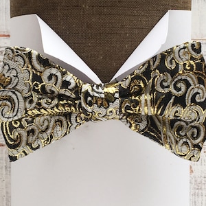 Puede incluir: Una pajarita negra con un patrón paisley dorado y blanco.