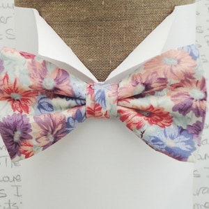 May include: A floral patterned bow tie with pink, red, purple, and blue flowers on a white background.