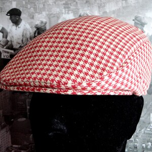 Op de afbeelding: Een rode en witte pied-de-poule pet. De pet is gemaakt van een geweven stof en heeft een ronde kroon en een kleine, stijve klep. De pet is een klassieke stijl, vaak geassocieerd met vintage of retro mode.