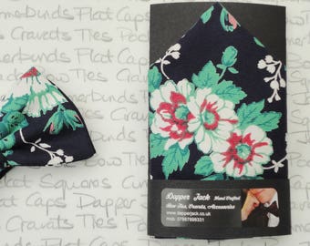 Può includere: Un papillon blu navy con un motivo floreale bianco e verde. Il papillon è mostrato accanto a un fazzoletto da taschino con lo stesso motivo. Il fazzoletto da taschino è confezionato con una carta che dice "Dapper Jack Hand Crafted Bow Ties, Cravats, Accessories www.dapperjack.co.uk mob: 07887898331"